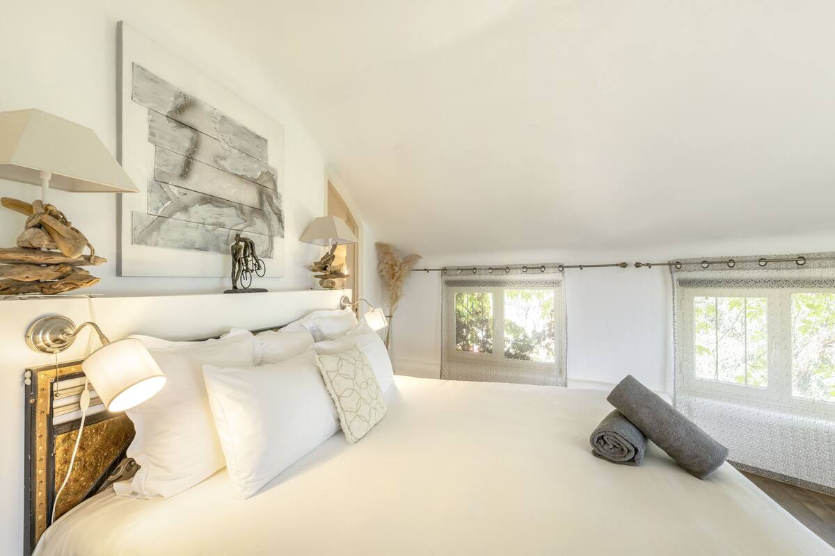 A bedroom with a large bed, two wall-mounted lamps, a rustic headboard, and a window with curtains.