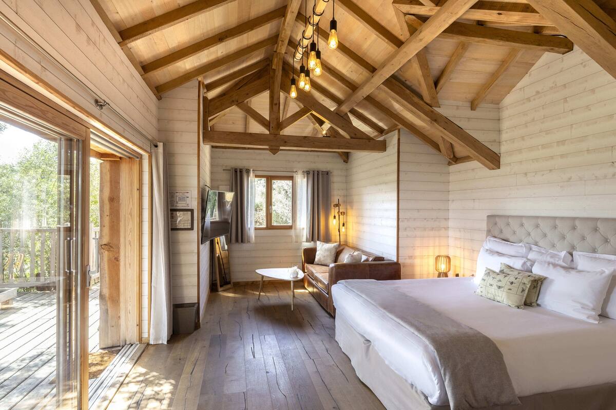 A wooden cabin interior with a bed, a sofa, a small table, and a TV.