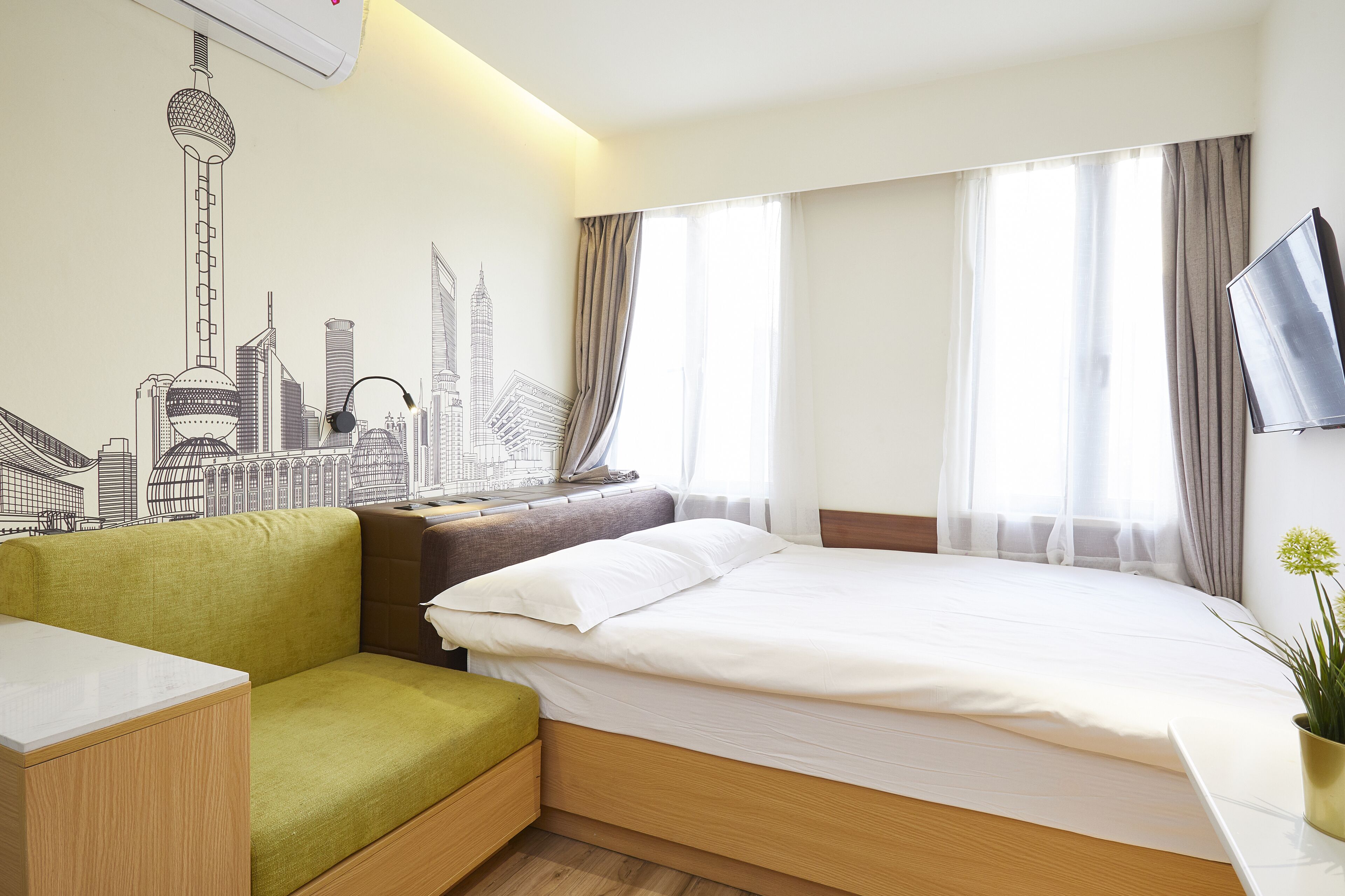 A hotel room with a bed, a green sofa, a small table, and a wall-mounted TV.