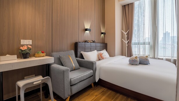 Habitación de hotel moderna con una pared de acento de madera, un sofá gris, un escritorio blanco y una cama grande con almohadones decorativos.