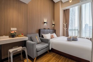 A modern hotel room with a wooden accent wall, a grey sofa, a white desk, and a large bed with decorative pillows. - Meego Youth Hotel Shanghai Jingan (Shanghai)