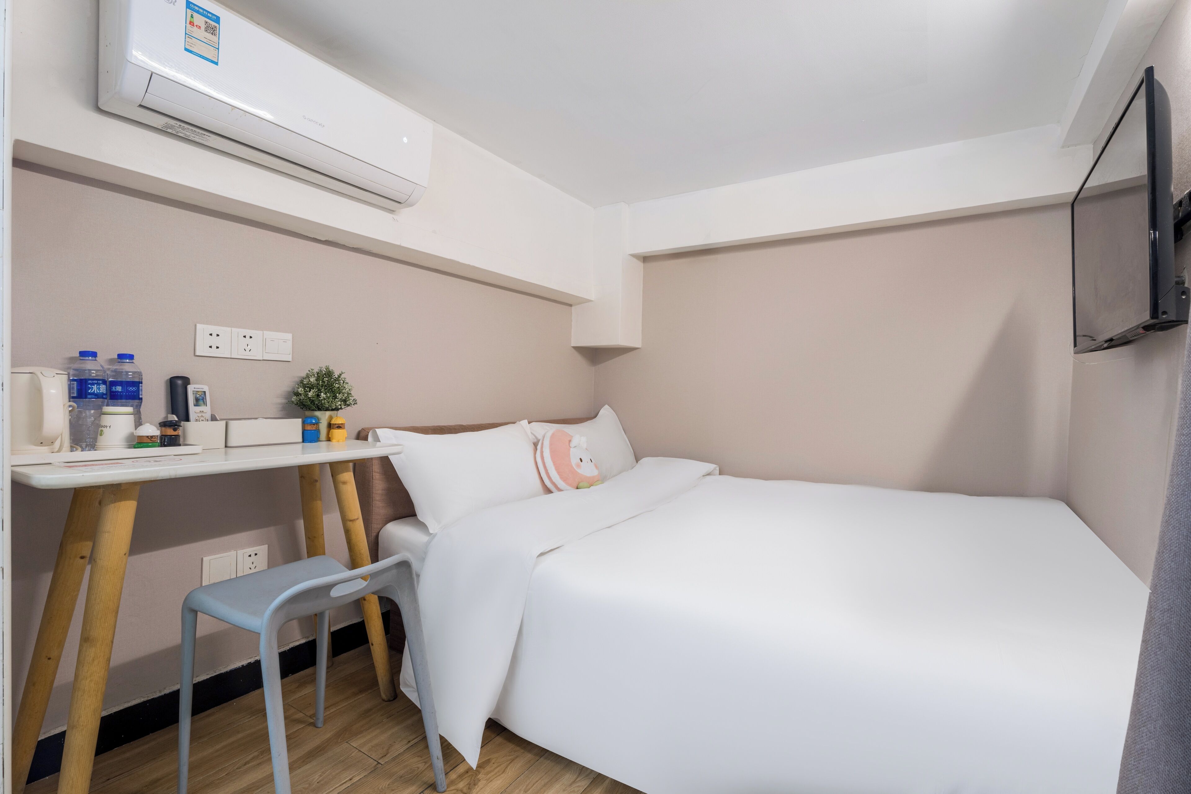 Una habitación pequeña y ordenada con cama, escritorio, silla, televisor y aire acondicionado.
