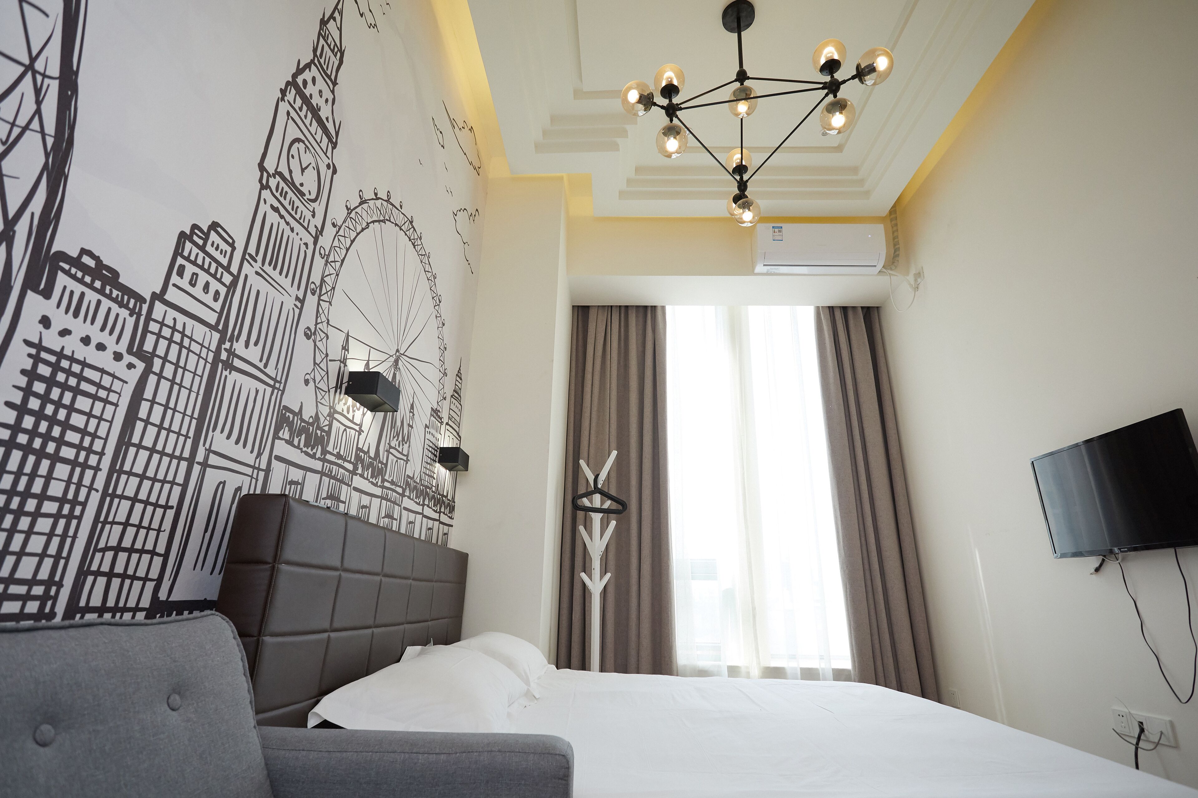 A hotel room with a large bed, a headboard, a wall-mounted TV, and a ceiling light fixture.