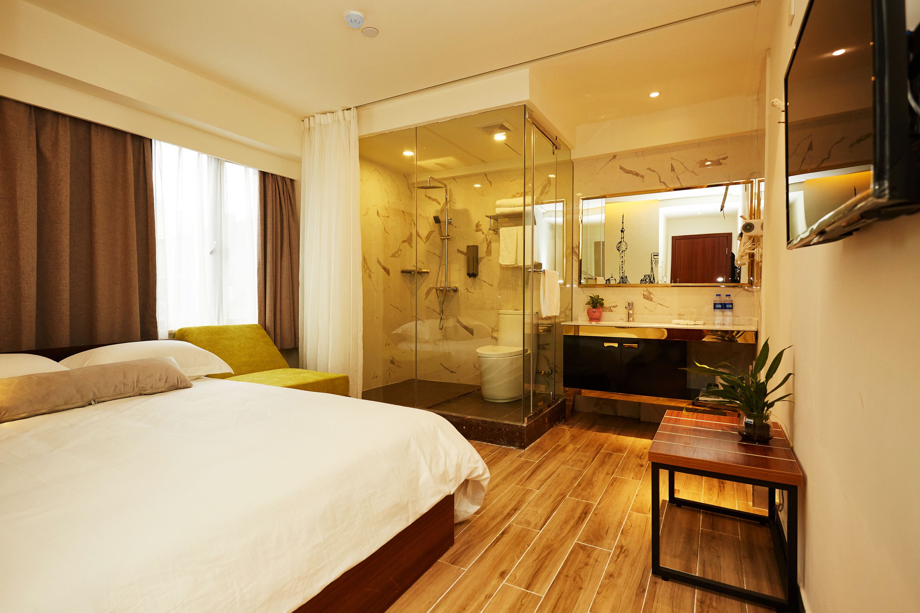A hotel room with a large bed, a glass-enclosed shower, a wooden floor, a small table, and a mirror.