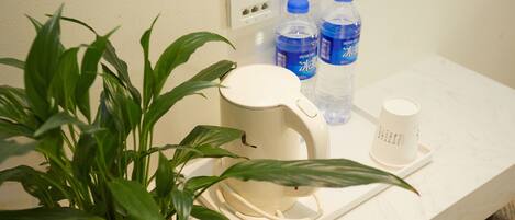 A kitchen counter with a kettle, two water bottles, a cup, and a potted plant.
