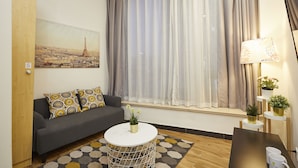 Una sala de estar moderna con un sofá gris, una mesa redonda de centro y un ventanal con cortinas translúcidas.