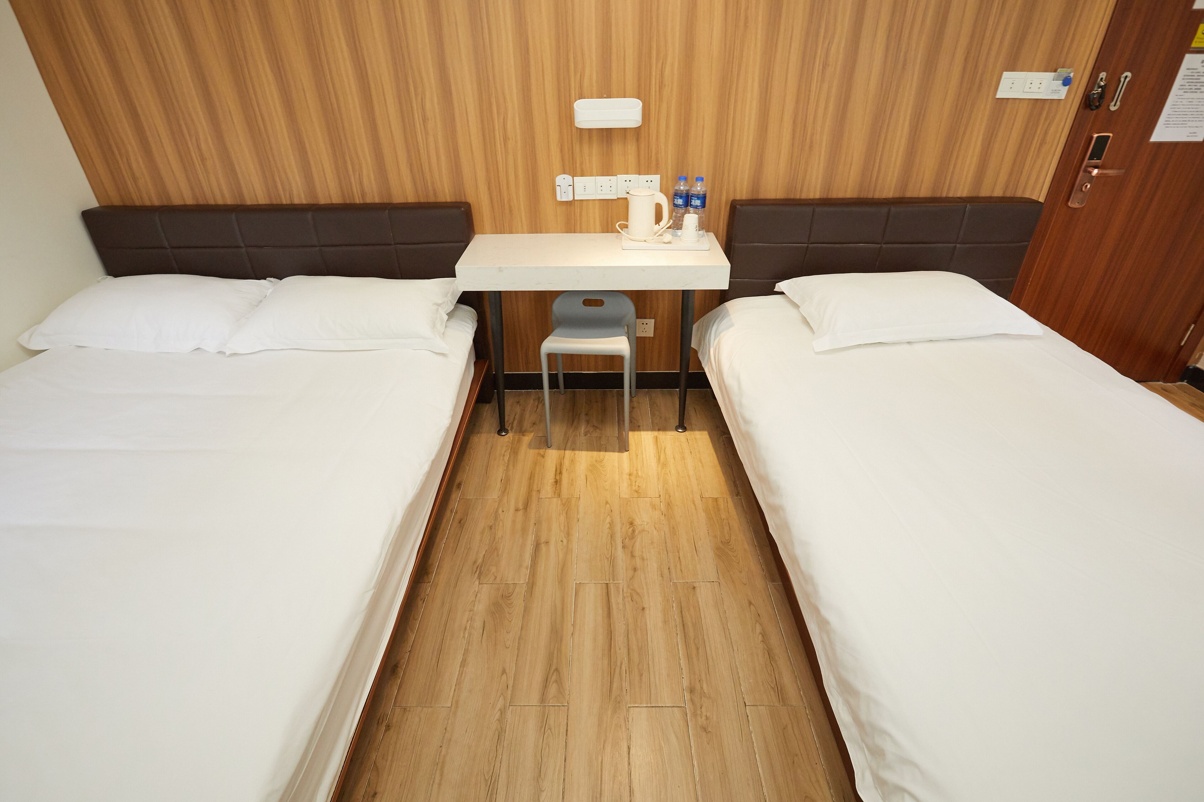 Une chambre d’hôtel avec deux lits, une petite table avec une chaise, une bouilloire et deux bouteilles d’eau.