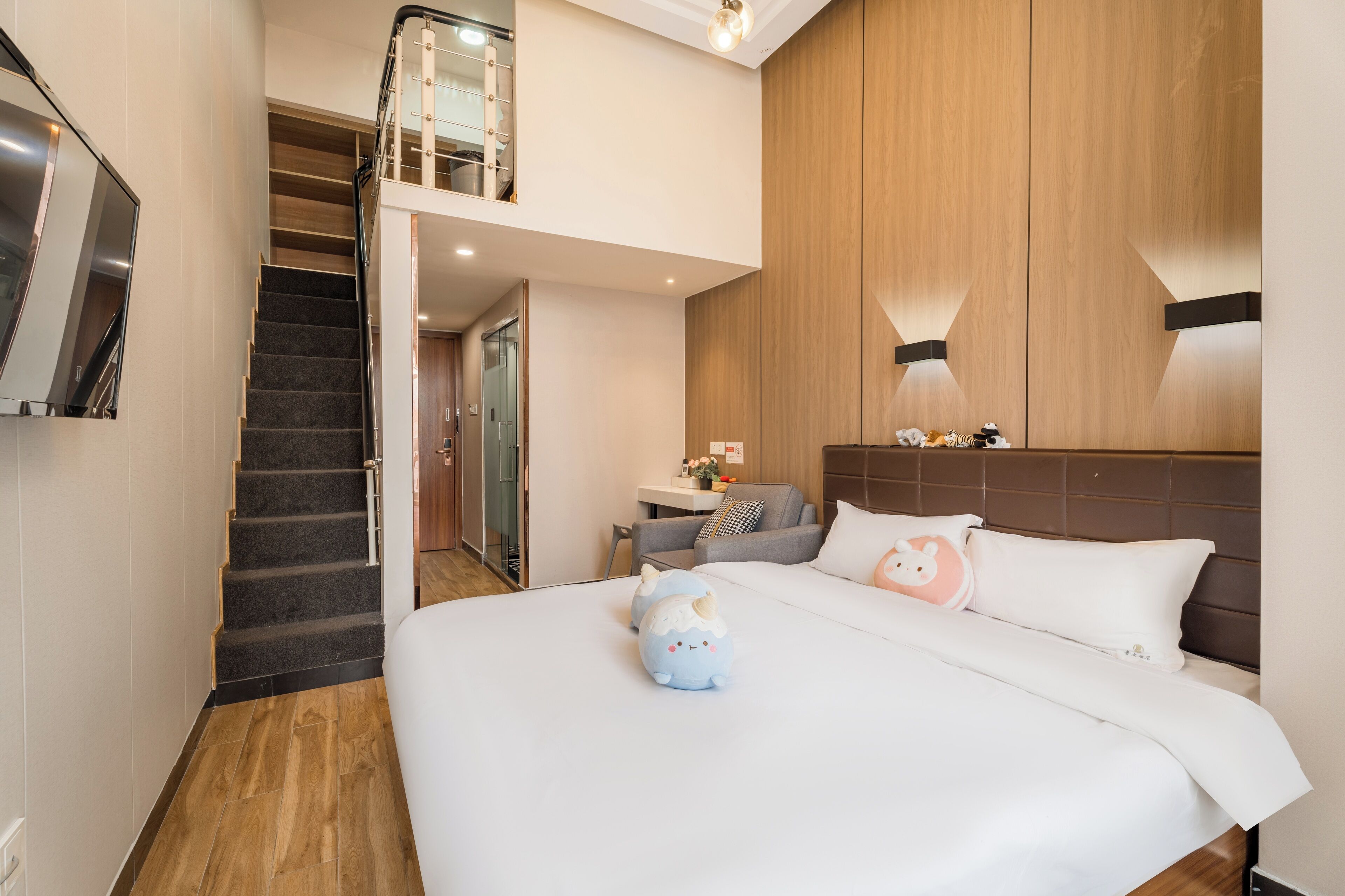 A hotel room with a large bed, a small desk, a sofa, and a staircase leading to an upper level.
