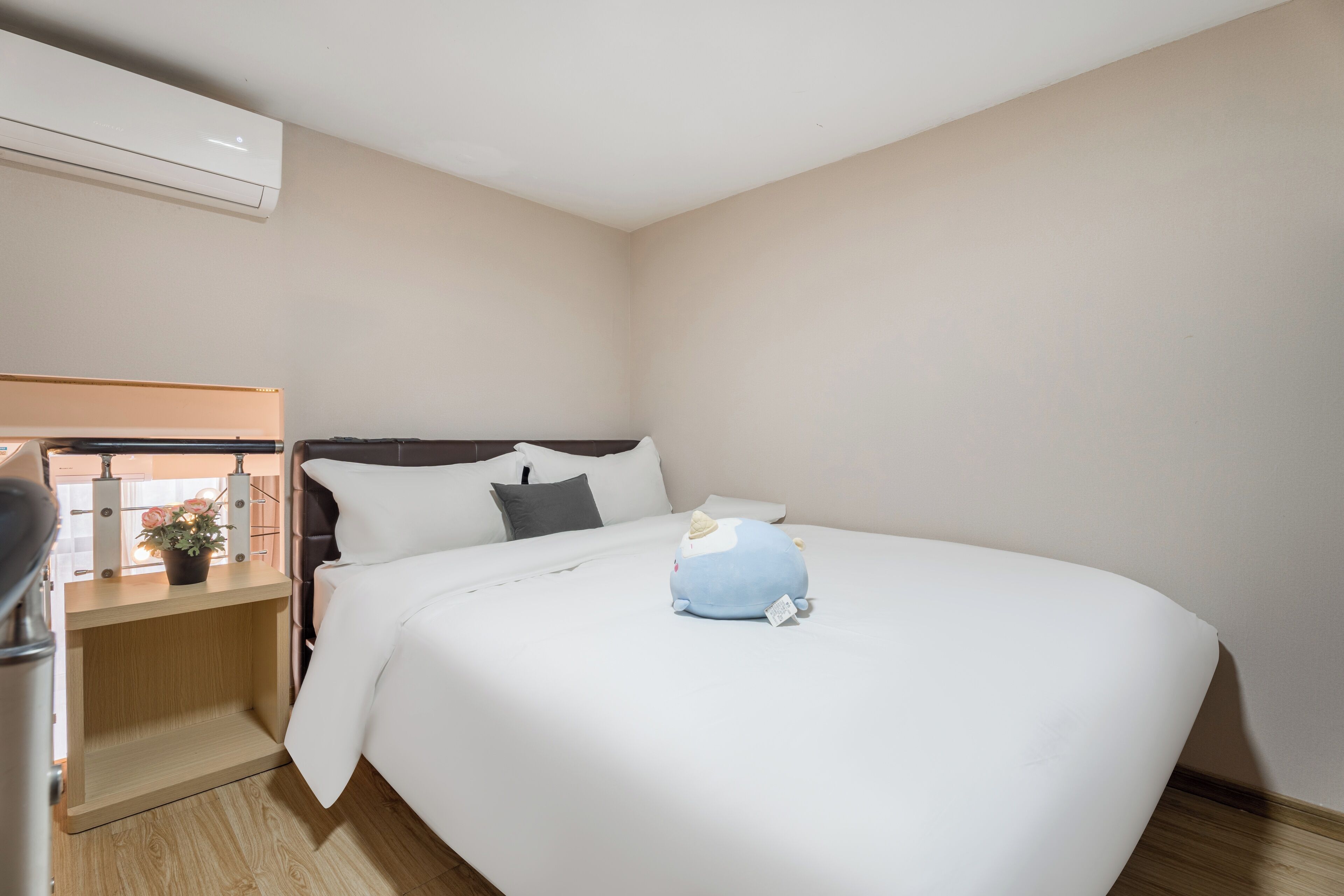 A hotel room with a large bed, a bedside table with a lamp, and a wall-mounted air conditioner.