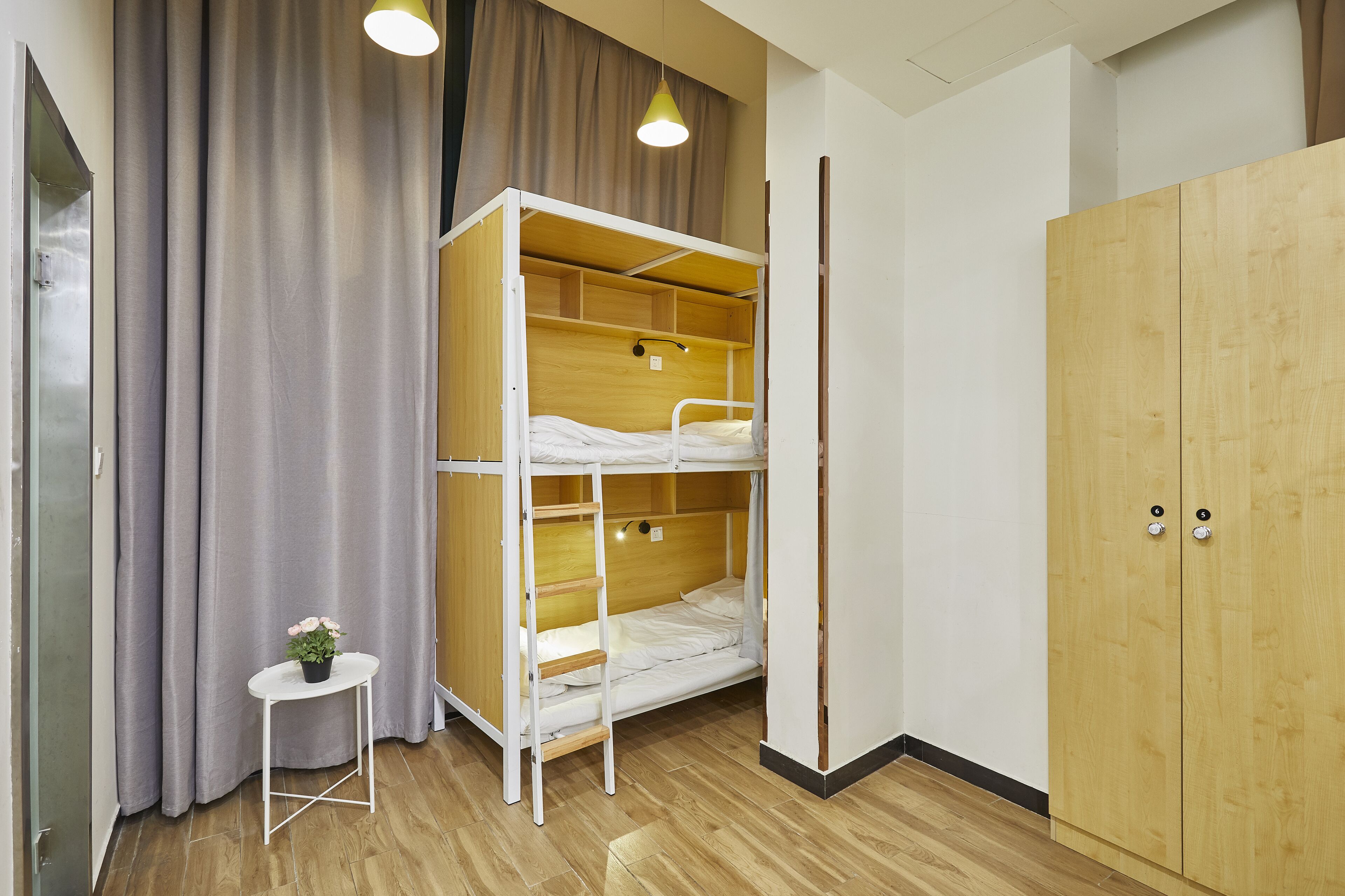 A bunk bed room with a wooden wardrobe, a small table with a plant, and a curtain.