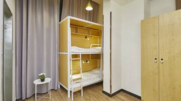 A bunk bed room with a wooden wardrobe, a small table with a plant, and a curtain.