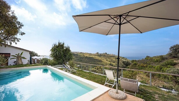 Una piscina con sillones de descanso y una sombrilla, rodeada de un jardín ajardinado y vistas al campo.