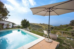A swimming pool with lounge chairs and an umbrella, surrounded by a landscaped garden and a view of the countryside.