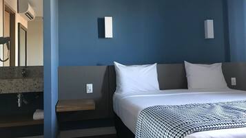 Habitación de hotel con cama, mesita de noche, espejo y baño con lavabo y toalla.