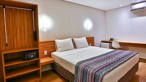 A hotel room with a bed, a desk, a chair, a wardrobe, and an air conditioning unit. - Maringá Airport Hotel (Maringá)