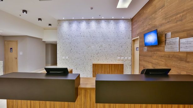 A reception area with a stone wall, wooden reception desk, and a mounted television. - Maringá Airport Hotel (Maringá)