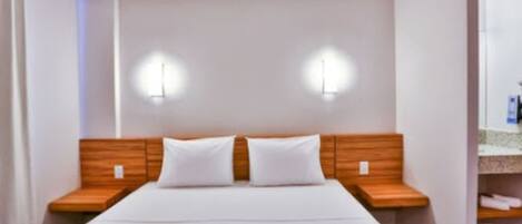Una habitación de hotel con cama, cabecero de madera, dos mesitas de noche y lámparas de pared.