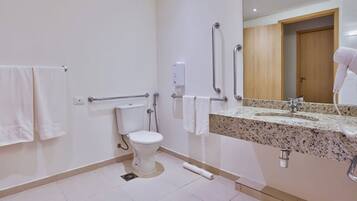A bathroom with a toilet, grab bars, a hand dryer, and a sink with a mirror.