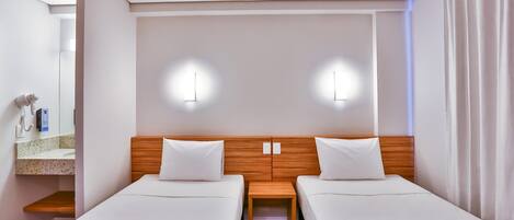 Habitación de hotel con dos camas individuales, cabecera de madera, mesita de noche de madera, un espejo y un secador de pelo en la pared.
