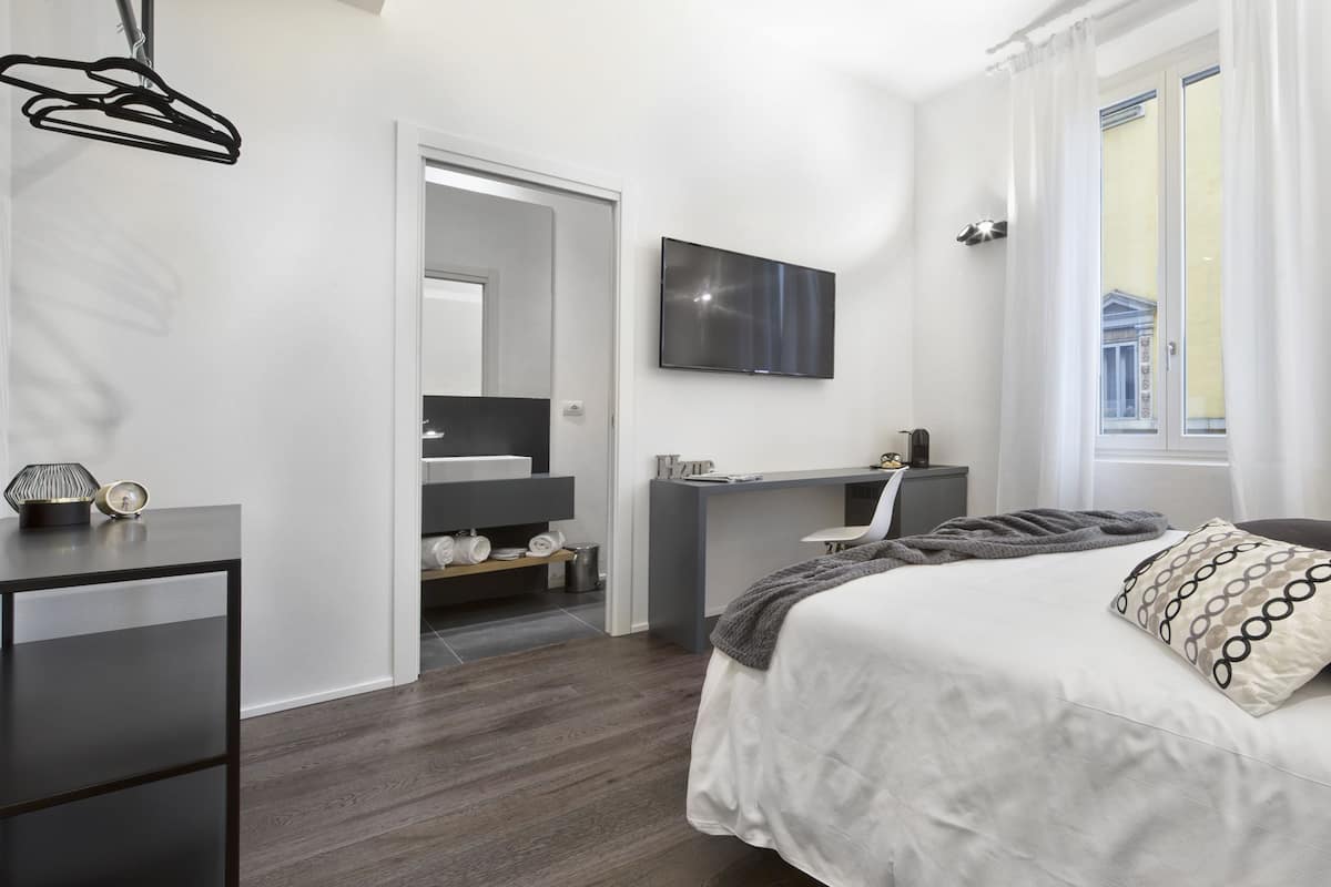 Un dormitorio moderno con cama, mesita de noche y televisor montado en la pared.