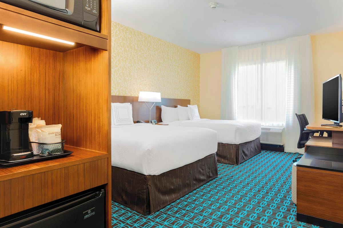 A hotel room with two beds, a desk with a computer, a coffee maker, and a microwave on a shelf.