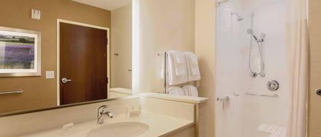 A hotel bathroom with a large mirror, a sink, a shower, and a towel rack.
