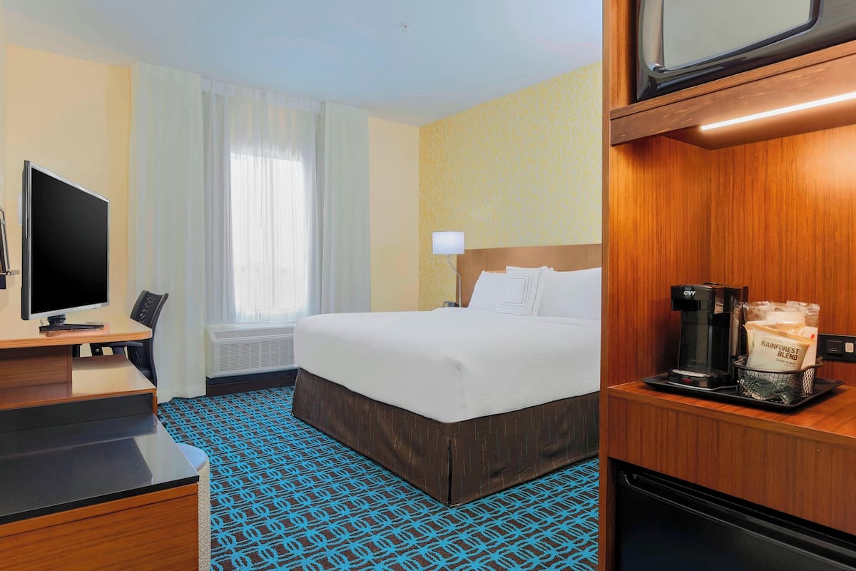 A hotel room with a bed, a desk with a TV, a coffee maker, and a bag of coffee.