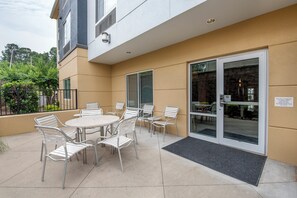 An outdoor patio with a round table and chairs, a glass door entrance, and a black mat at the door.