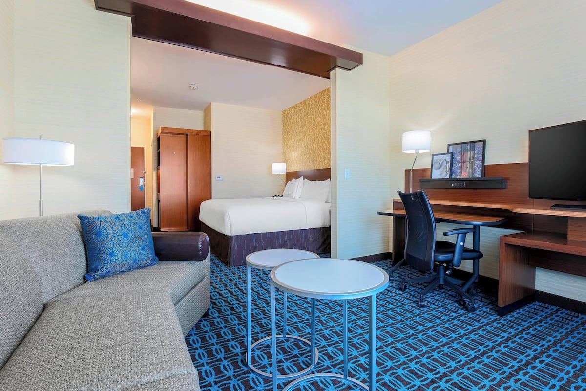 A hotel room with a bed, a desk, a chair, a sofa, and two small tables.