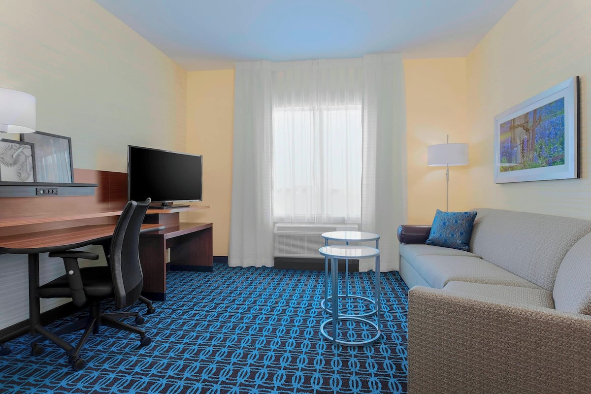 A hotel room with a desk, chair, television, sofa, and a patterned carpet.