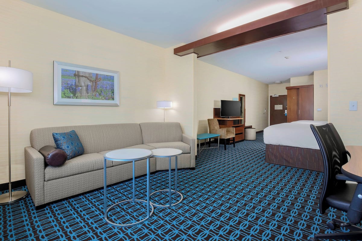 A hotel room with a sofa, two small tables, a TV, a bed, and a patterned carpet.