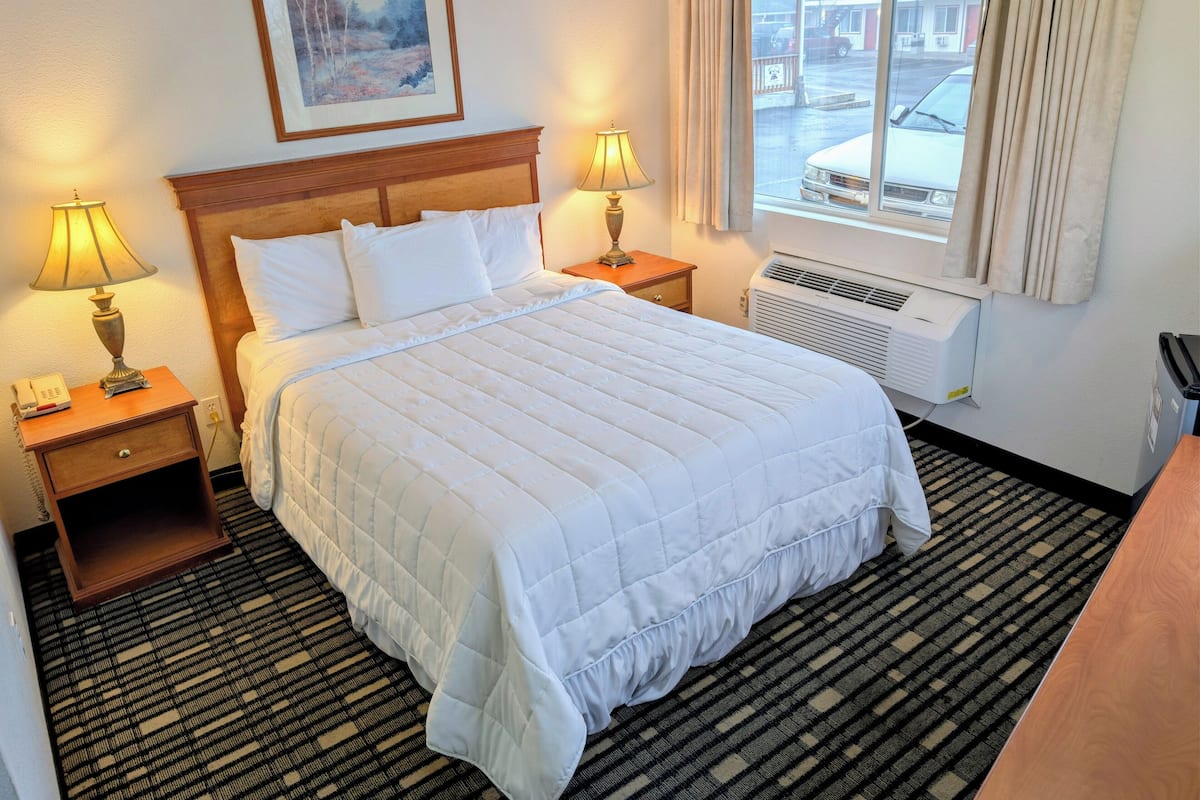 A hotel room with a large bed, two bedside tables with lamps, a painting on the wall, and a window with curtains.