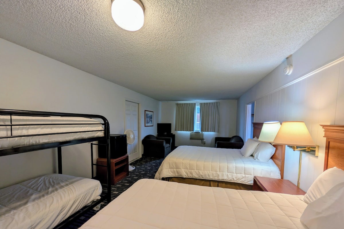 A hotel room with two beds, a desk, a chair, a TV, and a lamp.