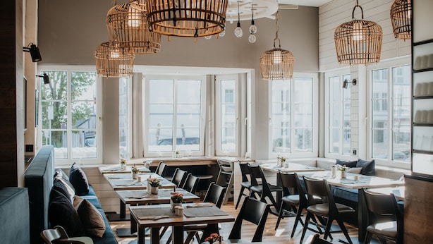 A modern dining area with high ceilings, large windows, and wicker pendant lighting.