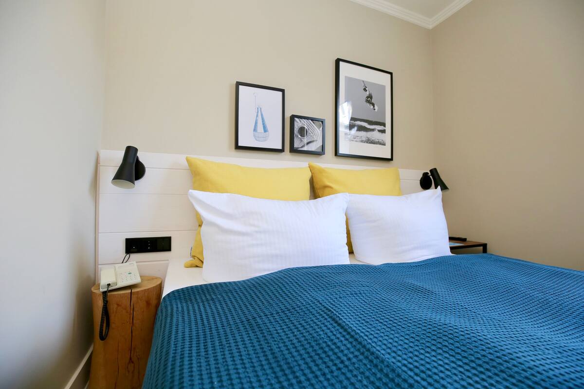 A hotel room with a bed, a bedside lamp, a phone, and framed pictures on the wall.