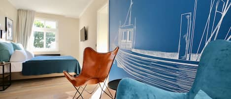 A bedroom with a bed, a chair, a large window, and a wall mural.