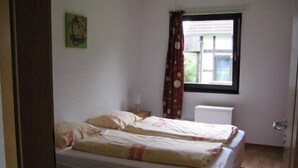 Una habitación pequeña con cama individual, ventana, radiador y puerta.