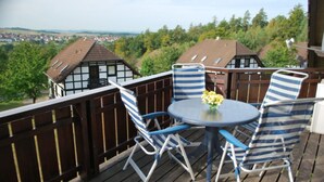 Terraza de madera con una mesa redonda y sillas a rayas, con vistas a un pueblo con casas tradicionales.