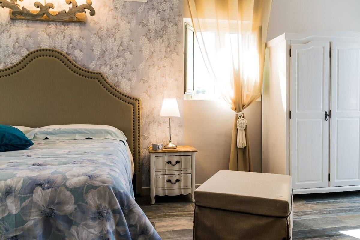 A bedroom with a bed, bedside table, lamp, curtains, and wardrobe.