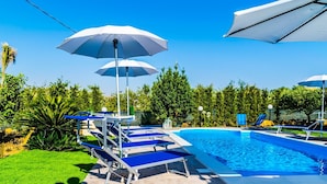 Ein Swimmingpool mit Liegestühlen und Sonnenschirmen, umgeben von viel Grün.