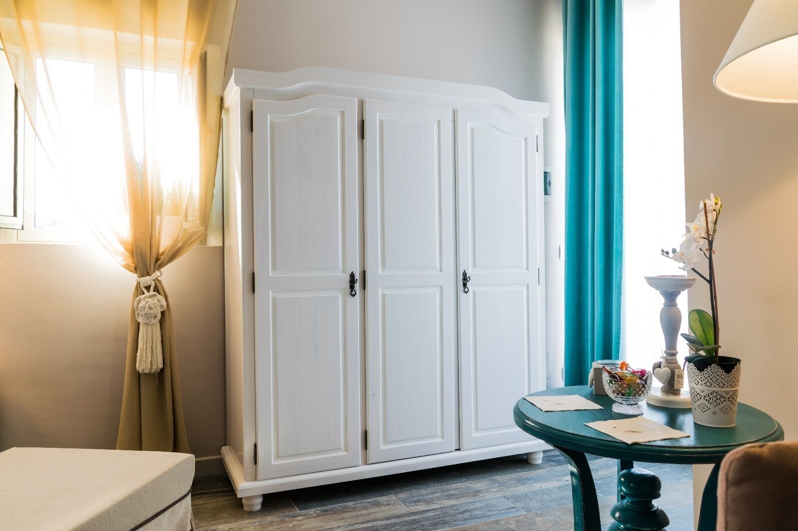A room with a white wardrobe, a round table with a teal tablecloth, and a potted orchid.