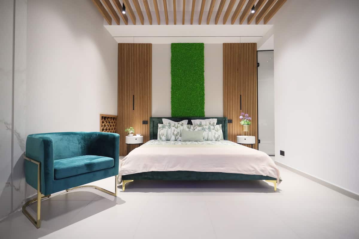 A modern bedroom with a bed, a blue armchair, wooden panel walls, and a green vertical garden.