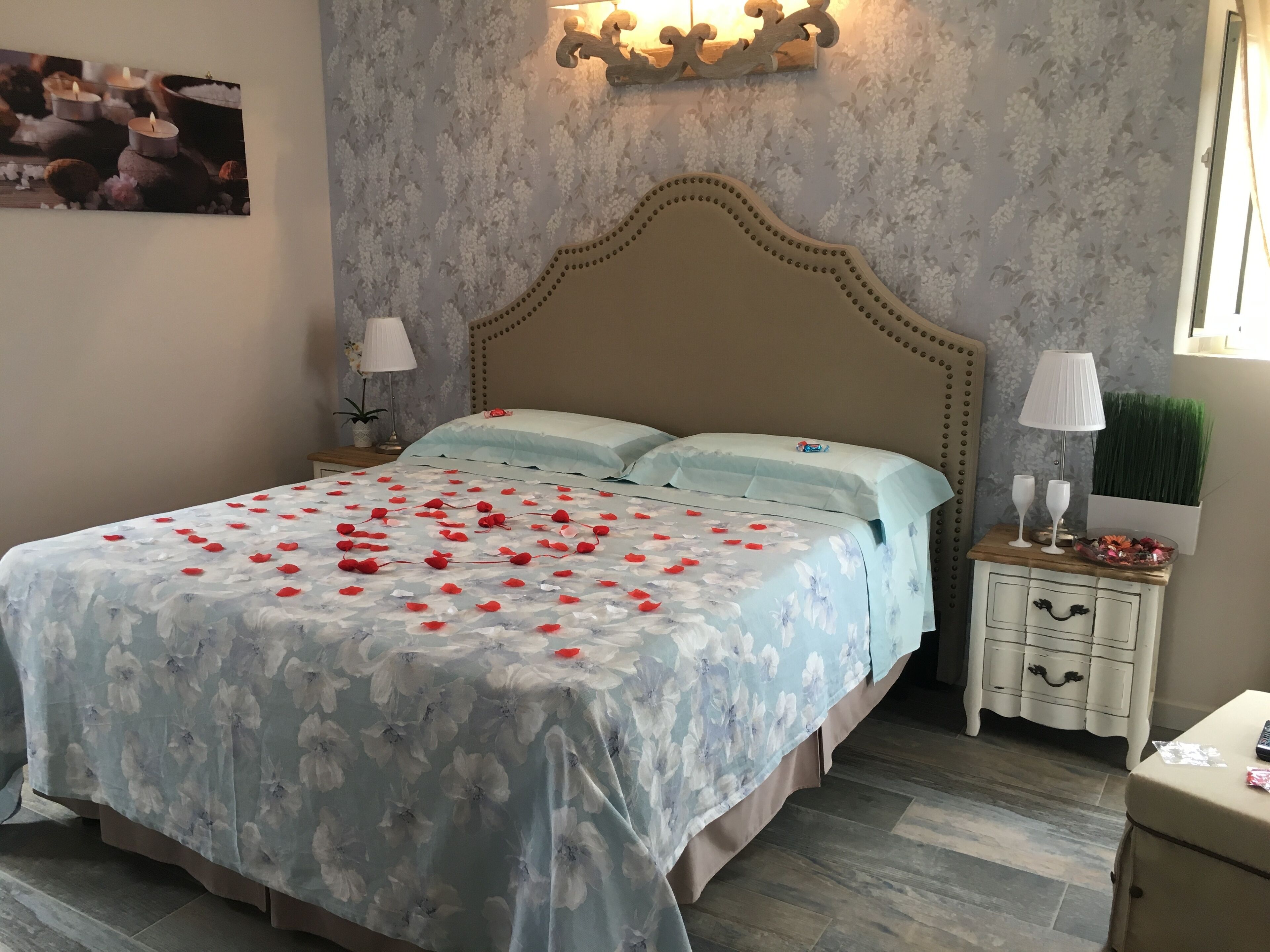 A bedroom with a floral bedspread, a decorative headboard, bedside tables with lamps, and a wall-mounted light fixture.