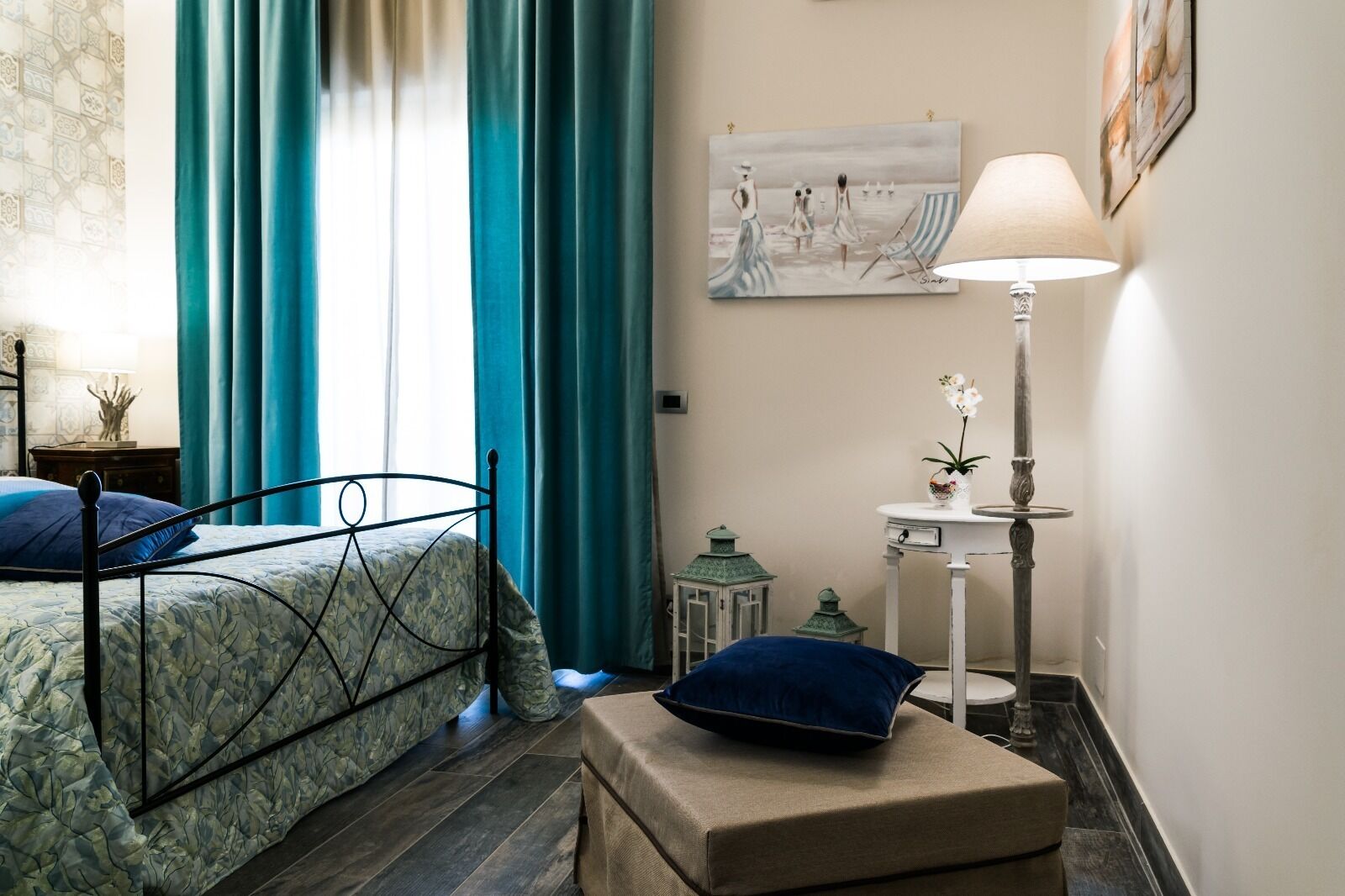 Een slaapkamer met een bed, nachtkastje, lamp en een schilderij aan de muur.