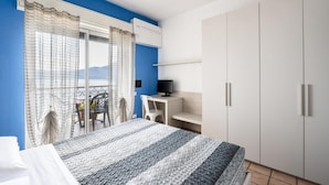 A bedroom with a bed, a desk, and a TV. There is a balcony with a chair and a table.