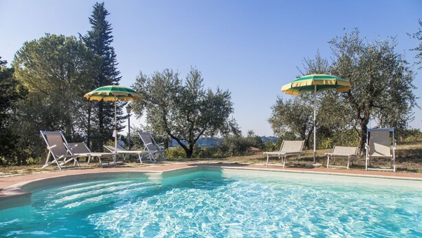 A swimming pool with clear blue water, surrounded by lounge chairs and umbrellas, set against a backdrop of trees and a clear sky. - Lilla - Two Bedroom Apartment, Sleeps 6 (Poggibonsi)