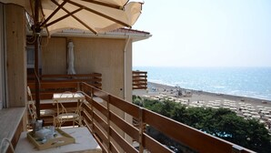 Varanda com vista para a praia, móveis de madeira e uma mesa com uma bandeja de objetos.