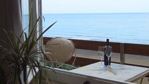 Uma mesa com uma garrafa, um copo, uma planta e vista para o mar.