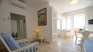 Uma sala de estar espaçosa com uma grande janela, uma área de jantar com mesa e cadeiras, e um espaço de estar aconchegante com sofá e poltronas.