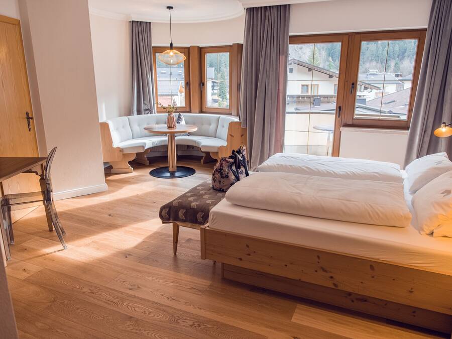 A bedroom with a wooden bed, a round table, a sofa, and large windows.